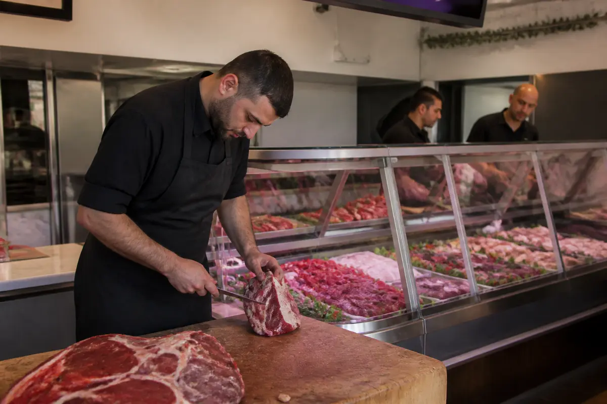 Boucher découpant de la viande dans une boucherie halal La Basse Côte de la Roseraie