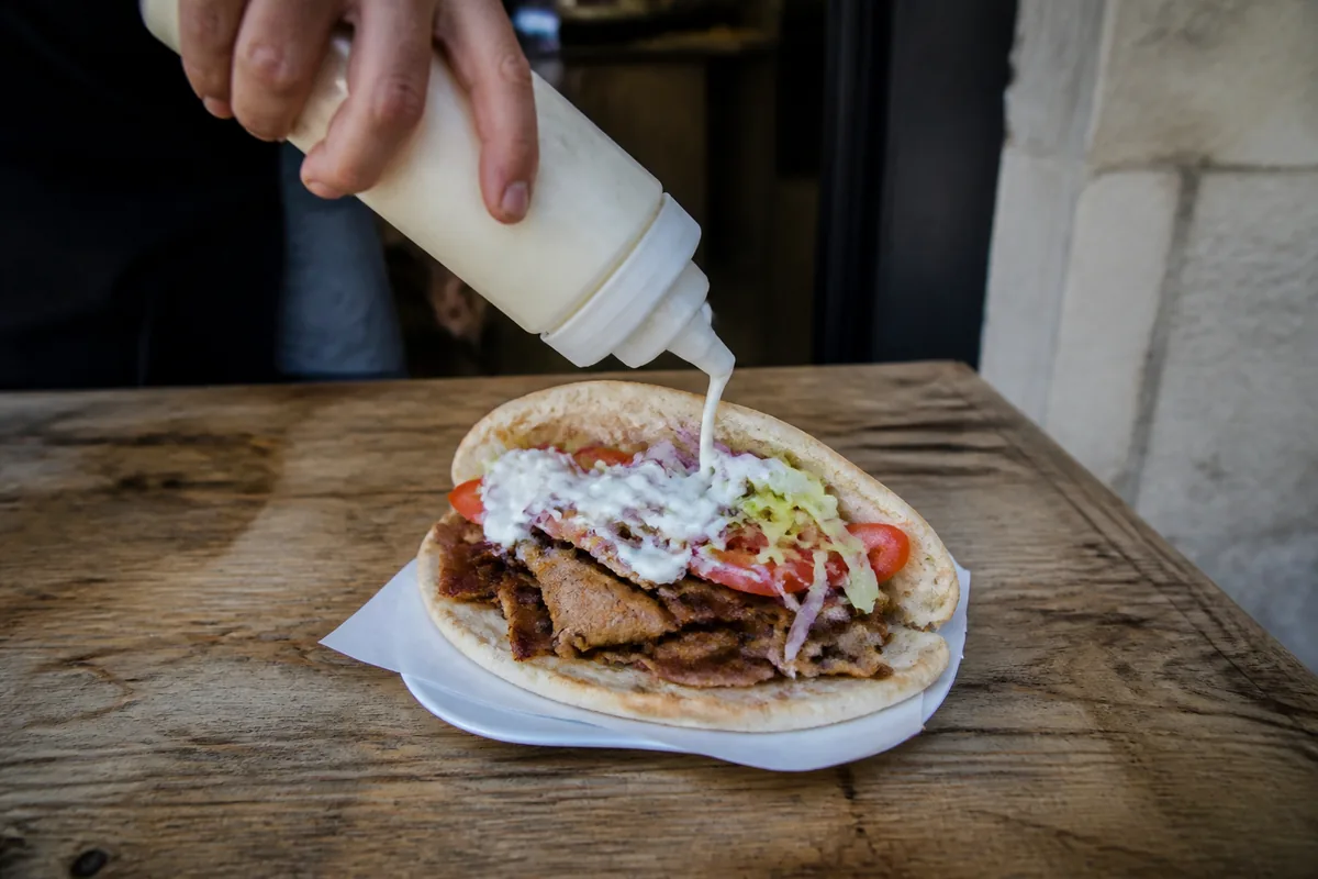 Sauce blanche versée maison sur un kebab aux légumes et viande grillée
